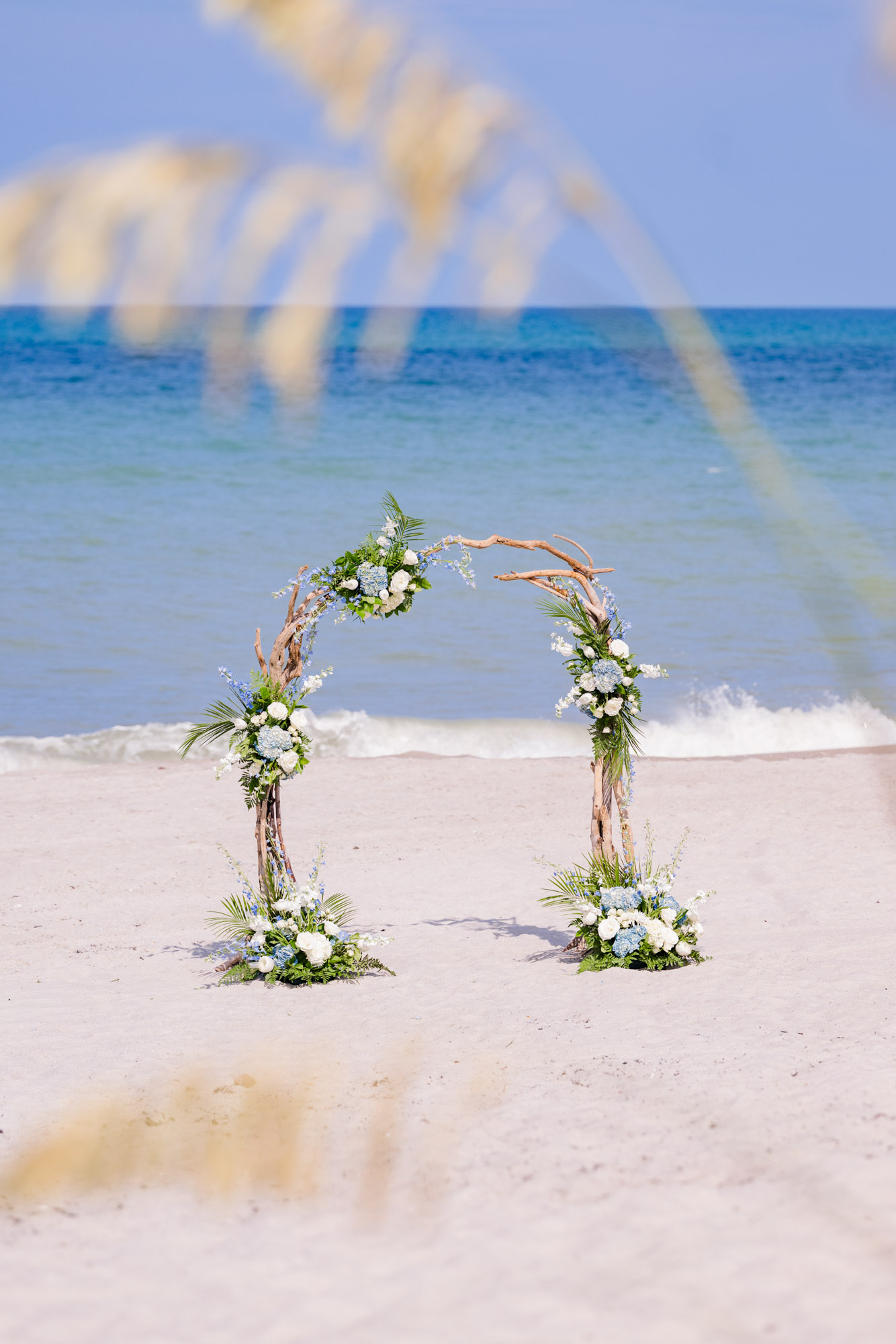 Driftwood wedding arch decorated with white roses and blue hydrangeas on the sand for a Melbourne Beach micro wedding.