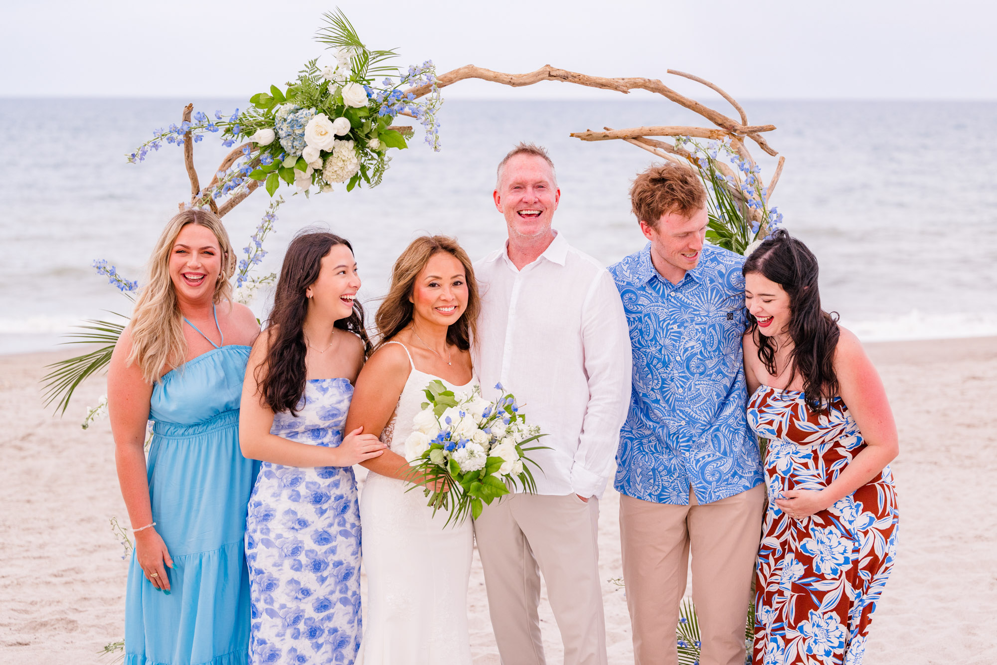 Bride and groom laughing with family during group wedding portraits on the beach in Melbourne Beach, Florida.