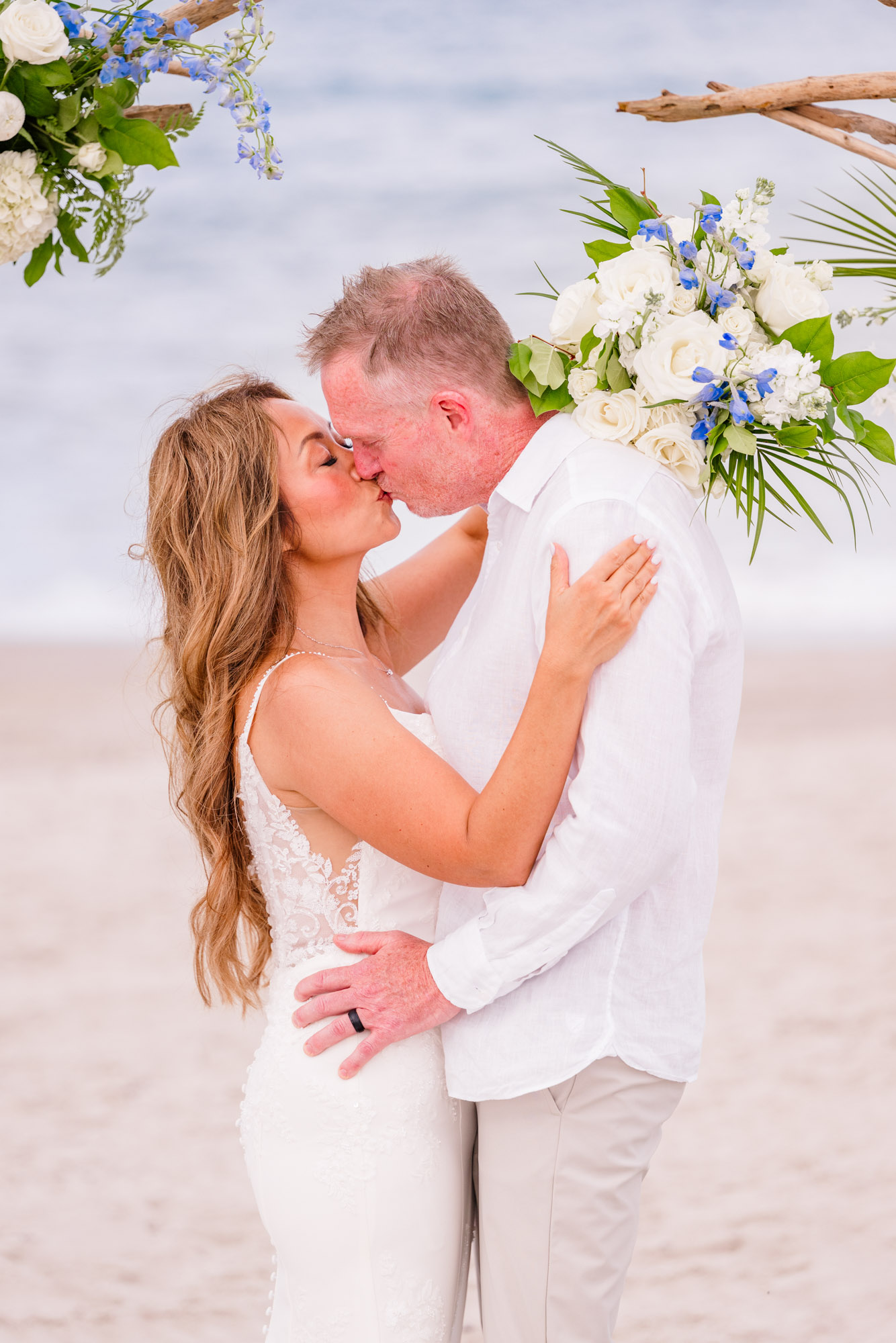 Close-up of newlyweds sharing a kiss beneath their blue and white floral wedding arch on Melbourne Beach.