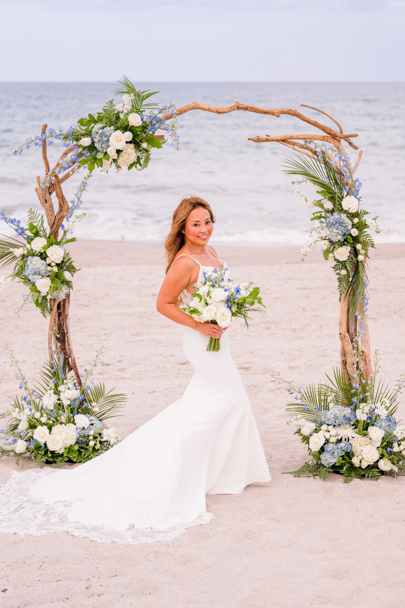 Bride holding her blue and white wedding bouquet beneath a floral arch during her intimate Melbourne Beach wedding.
