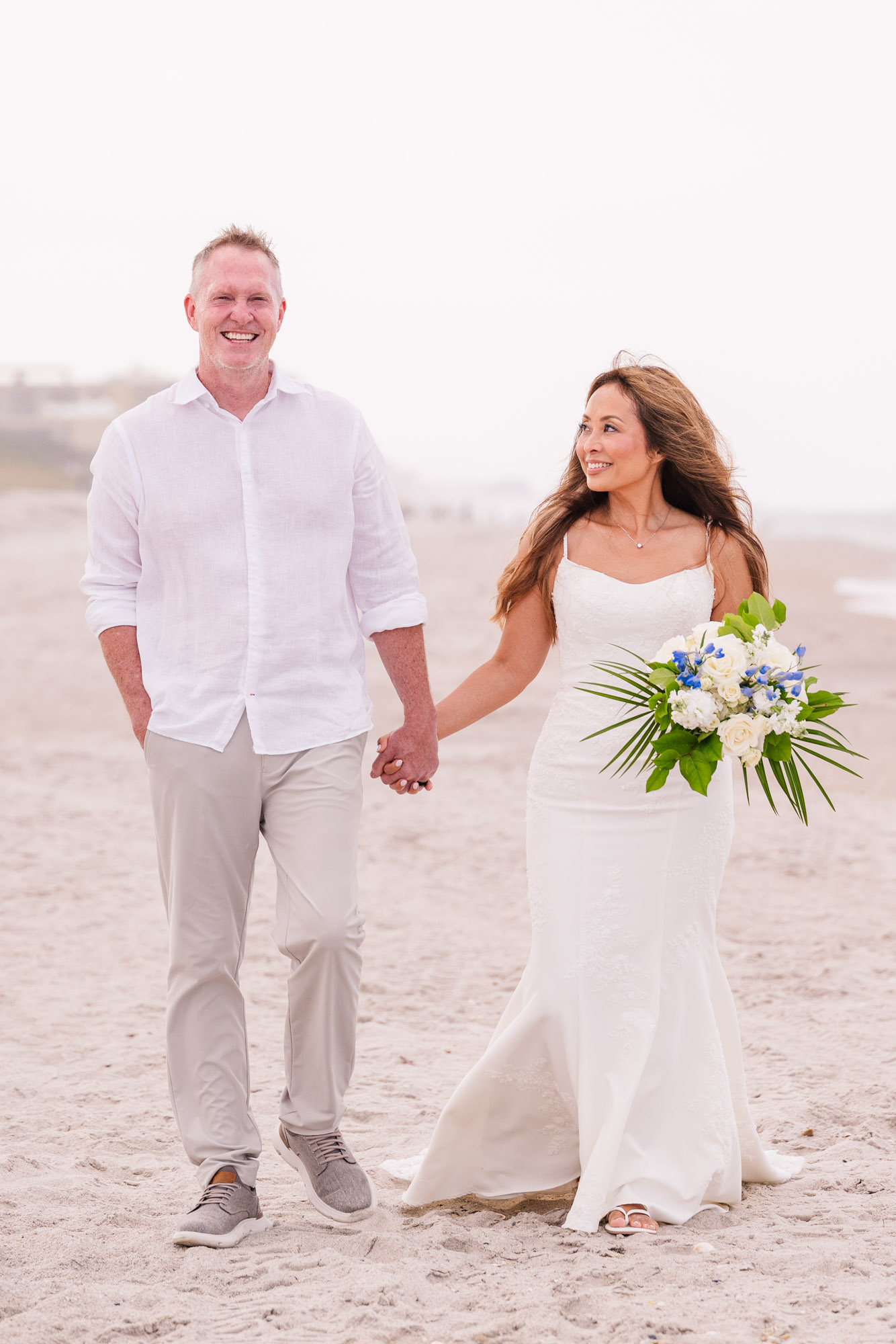 Newly married couple walking hand in hand along the shoreline after their small Melbourne Beach wedding.