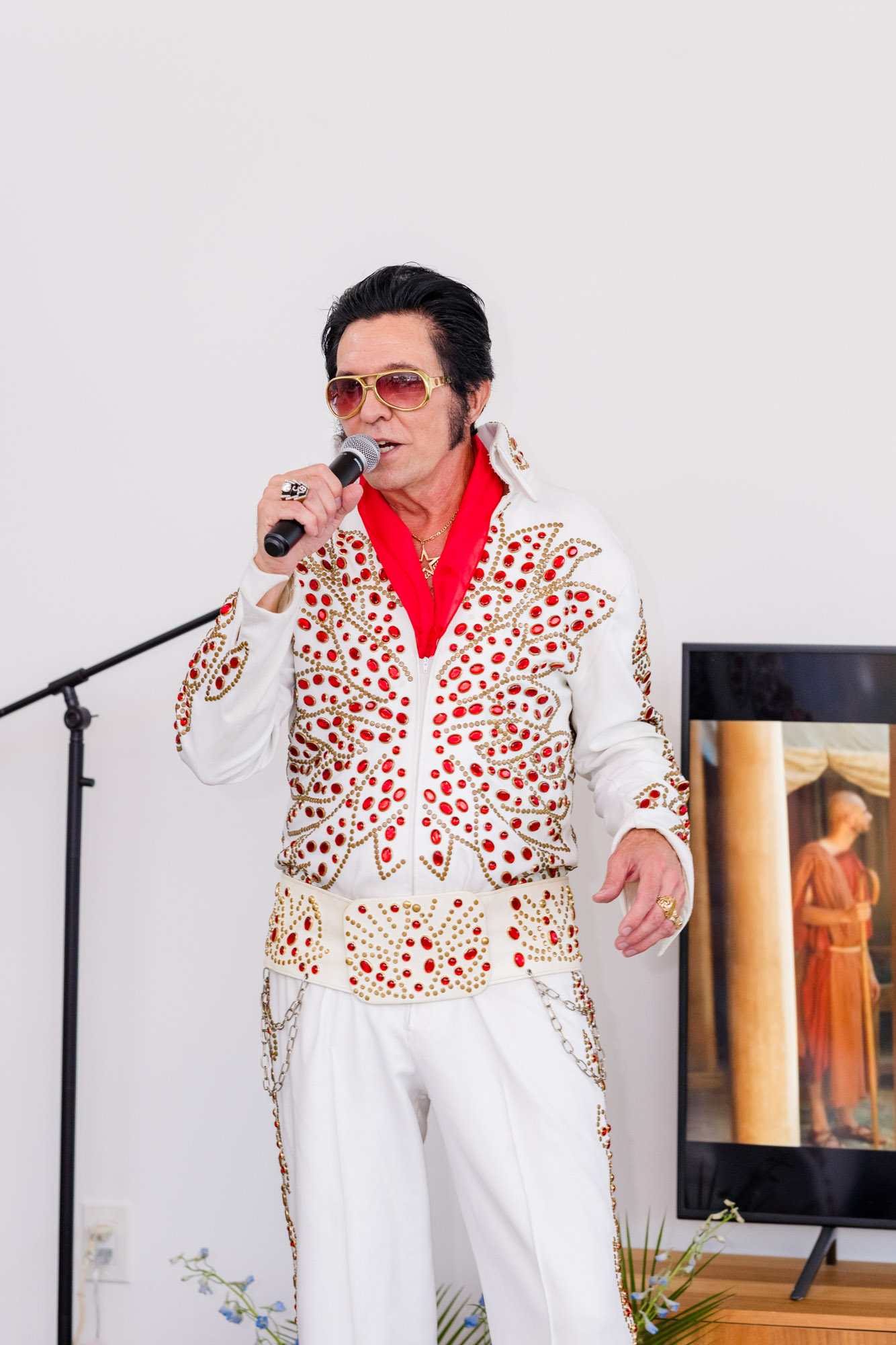Elvis impersonator singing into a microphone in a white and red jumpsuit at a Melbourne Beach micro wedding reception.