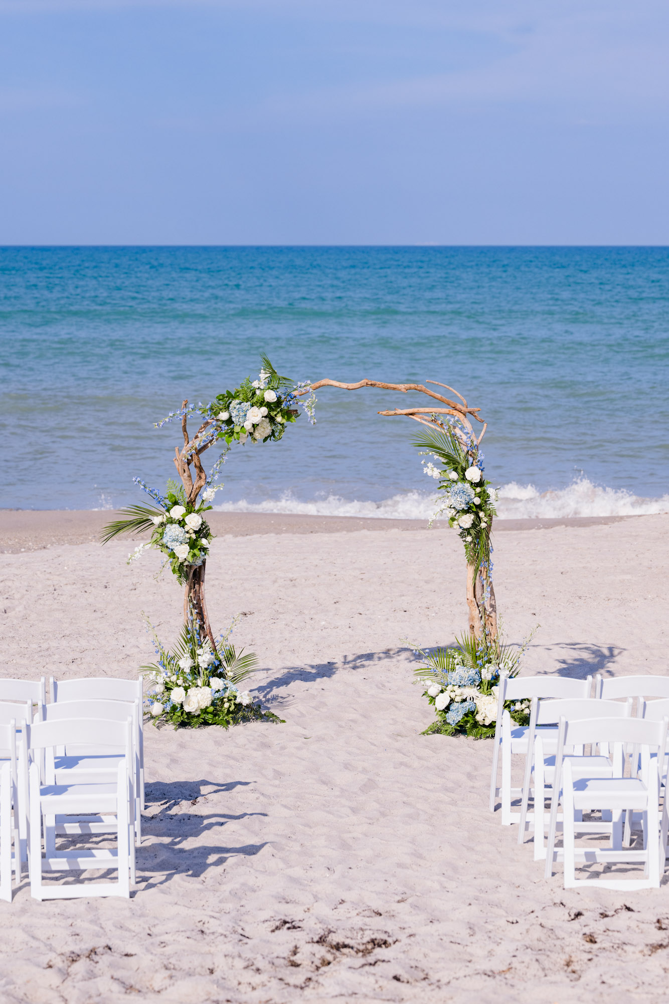 Intimate Melbourne Beach wedding ceremony setup with a floral driftwood arch and white guest chairs overlooking the Atlantic Ocean.