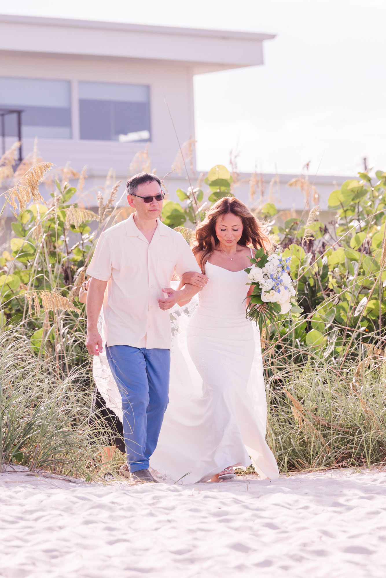 Bride in a white wedding gown walking through the beach dunes with her escort before her intimate Melbourne Beach wedding ceremony.