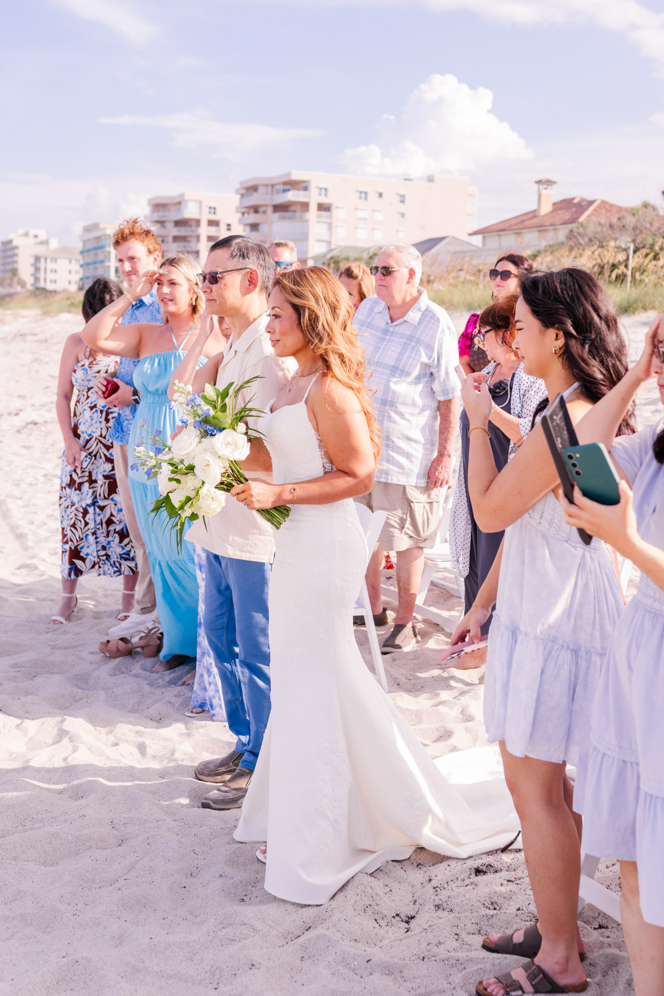 Bride holding a white and blue bouquet surrounded by family and guests before her Melbourne Beach wedding ceremony.
