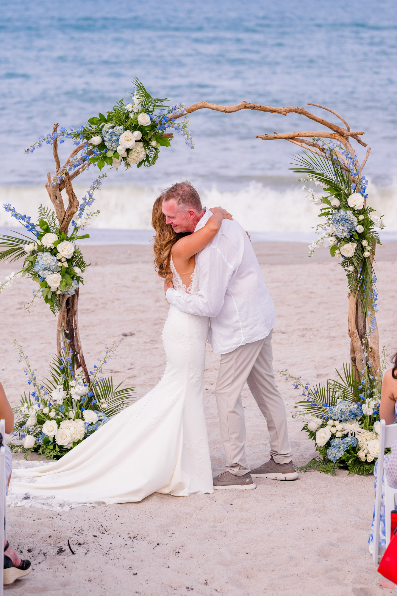 Newly married couple sharing an embrace beneath a floral wedding arch overlooking the ocean in Melbourne Beach.