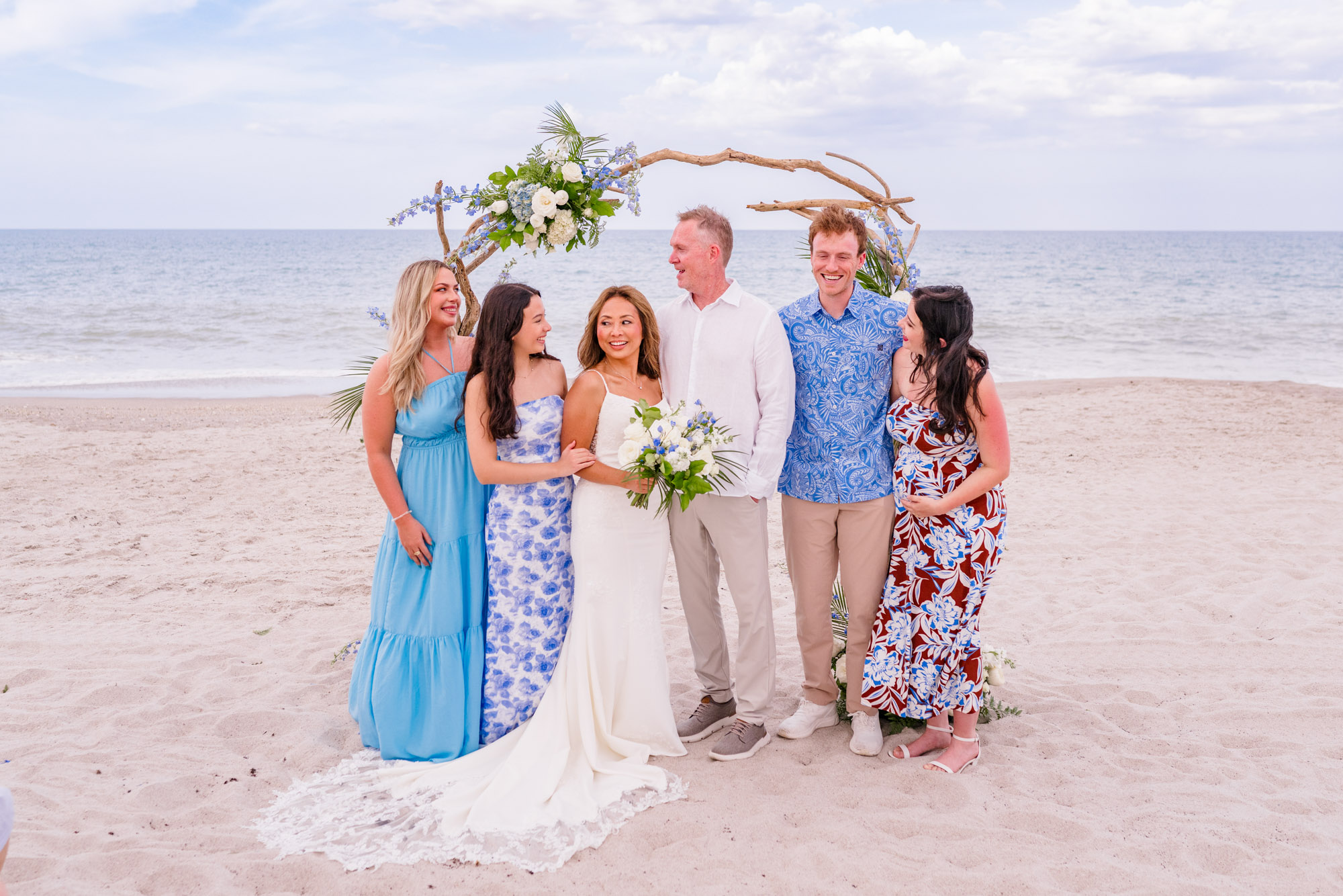 Newlyweds posing with family members beneath a driftwood arch after their intimate Melbourne Beach wedding ceremony.