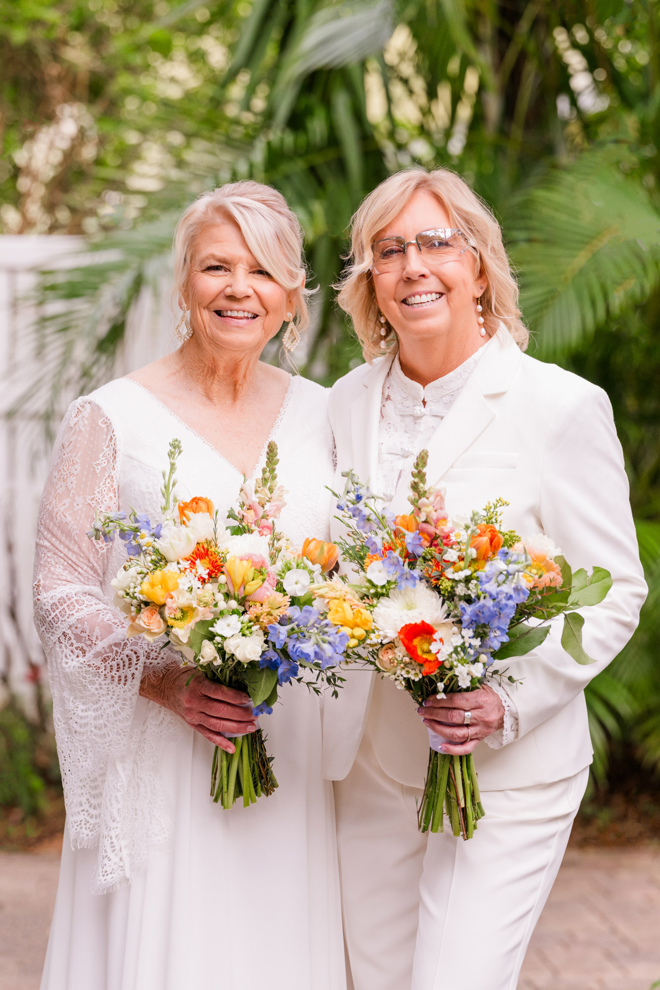 Two brides each holding bright tropical bouquets at their getting ready location in Melbourne Beach.