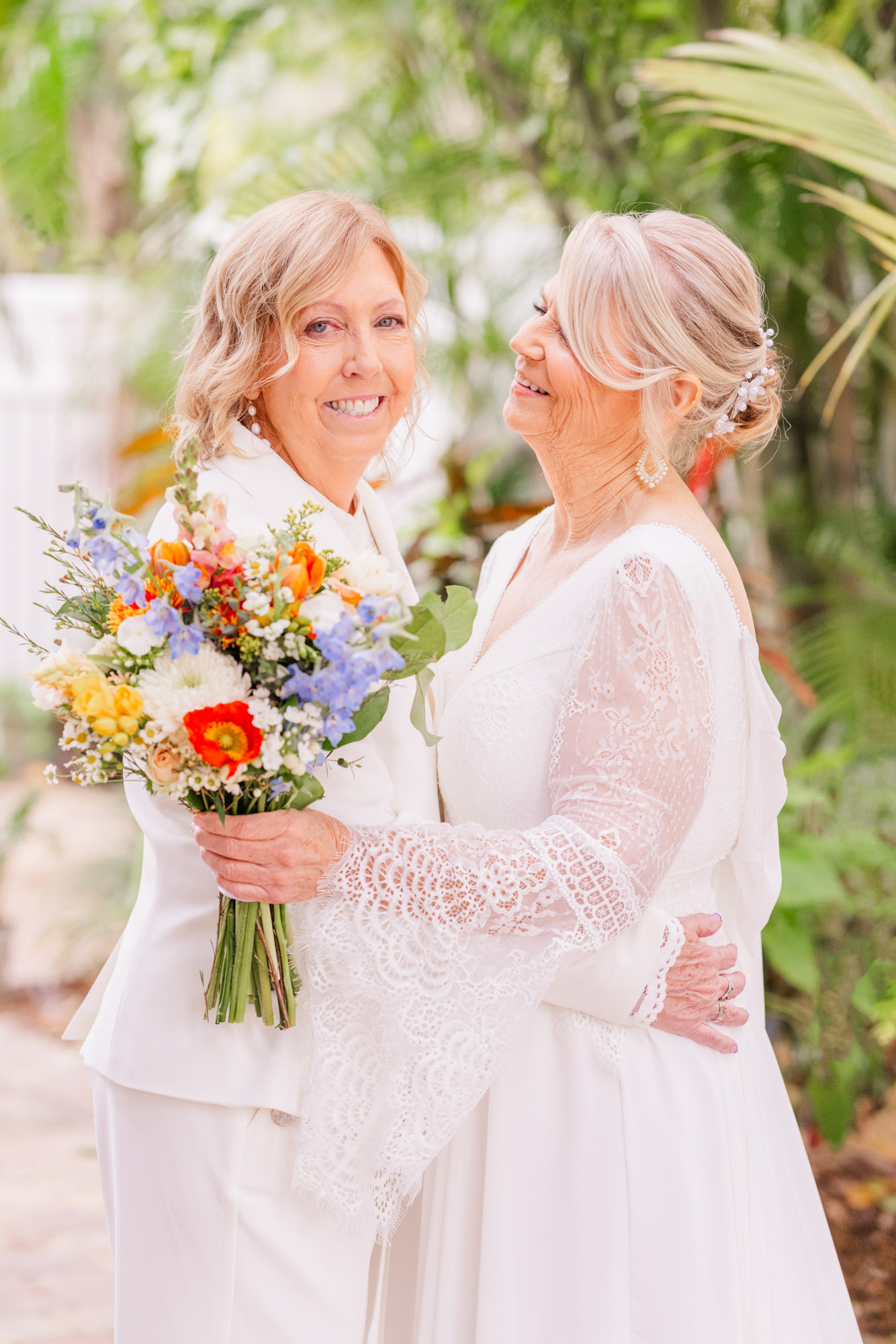 Two brides holding orange and yellow flowers hugging during their portrait session at the Seaglass Inn in Melbourne Beach