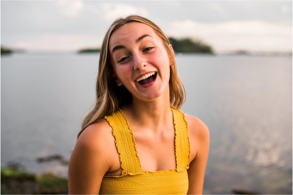 Girl in yellow top laughing at camera by the water