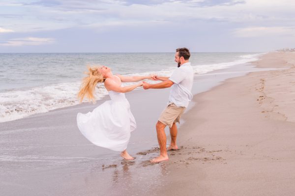 Man and women in a white dress spinning on the beach during an engagement session