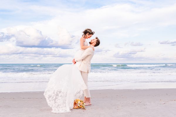 Groom lifting bride off the ground by the ocean in Florida after their wedding