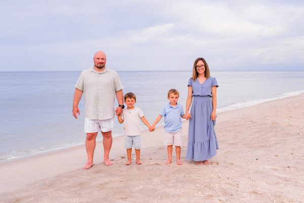 Family of four all holding hands walking down the beach with the little kids in the middle