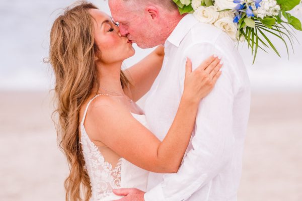 Close-up of newlyweds sharing a kiss beneath their blue and white floral wedding arch on Melbourne Beach.