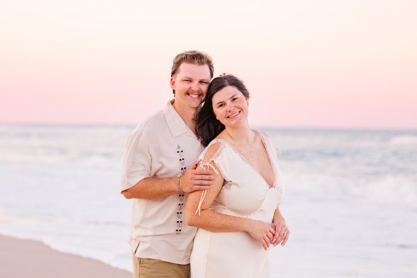 Man behind women on beach during a beautiful pink sunset